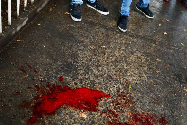 Anti-government protesters stand next to blood after a policeman was shot during clashes in Los Palos Grandes