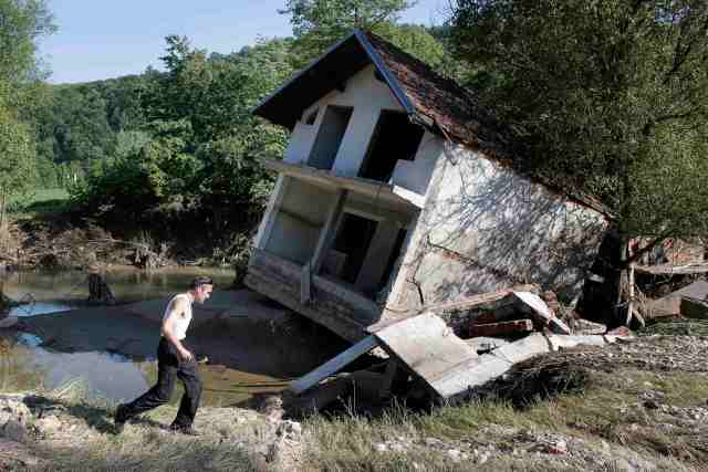 A man walks past a house tilted by floods in the town of Valjevo, southwest from Belgrade