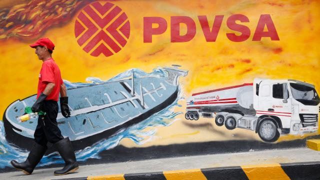 A worker walks past a mural with a PDVSA logo at its gas station in Caracas