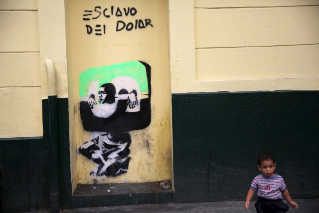 A boy walks next to graffiti that reads "Slave of the Dollar" in Caracas December 2, 2015. Venezuela will hold parliamentary elections on December 6. REUTERS/Nacho Doce