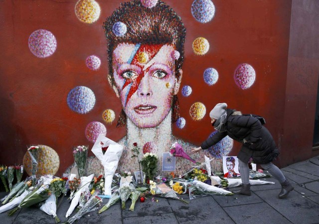 A woman leaves a bouquet at a mural of David Bowie in Brixton, south London, January 11, 2016. David Bowie, a music legend who used daringly androgynous displays of sexuality and glittering costumes to frame legendary rock hits "Ziggy Stardust" and "Space Oddity", has died of cancer.  REUTERS/Stefan Wermuth