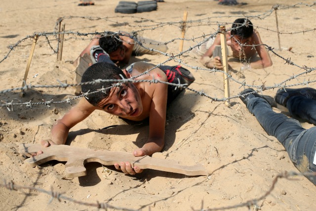 Los jóvenes palestinos Pasar por debajo de alambre de púas durante un ejercicio de estilo militar en un campamento de verano organizado por el Movimiento de la Yihad Islámica en Khan Younis, en el sur de la Franja de Gaza 13 de julio de 2016. REUTERS / Ibraheem Abu Mustafa
