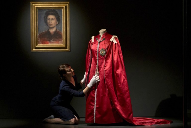 Un asistente posa con el Manto de la orden del vestido imperio británico de 1952, en la "configuración de una Reinado: 90 años de estilo a partir de la reina Armario", exposición en el interior de Buckingham Palace en Londres el 21 de julio de 2016. La exposición muestra una selección de trajes de la reina Isabel II, vestidos y accesorios en la celebración de su 90 cumpleaños. JUSTIN TALLIS / AFP 