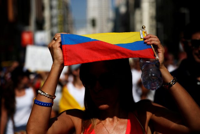 A protester shelters from the sun under a Venezuelan flag during a demonstration to demand a referendum to remove Venezuela's President Nicolas Maduro, in Madrid, Spain, September 4, 2016. REUTERS/Susana Vera