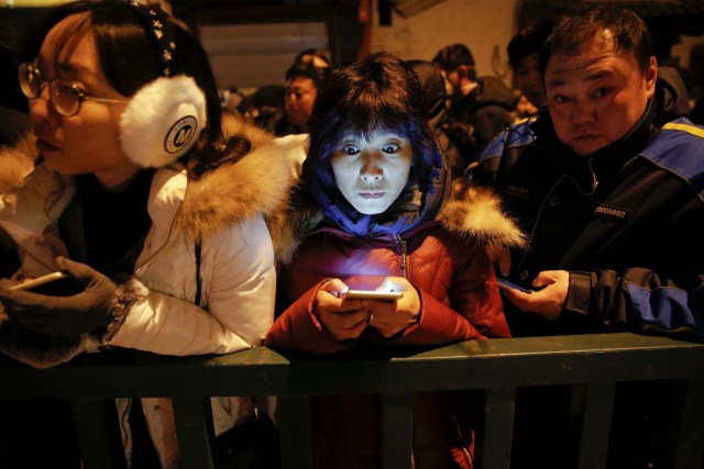 People use their phones as they wait for Yonghegong Lama Temple to open its gates so they can burn incense and pray for good fortune on the first day of the Lunar New Year of the Rooster in Beijing, China January 28, 2017. REUTERS/Damir Sagolj