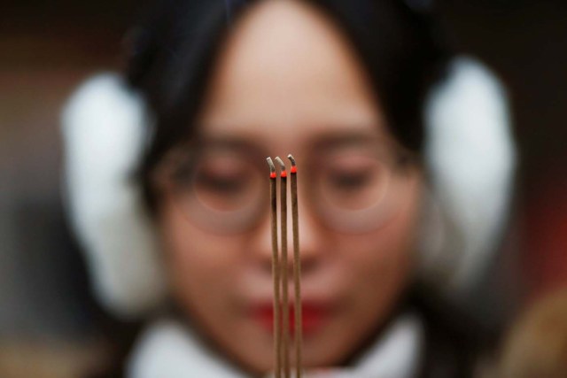 A woman holds incense sticks while praying at Yonghegong Lama Temple on the first day of the Lunar New Year of the Rooster in Beijing, China January 28, 2017. REUTERS/Damir Sagolj     TPX IMAGES OF THE DAY