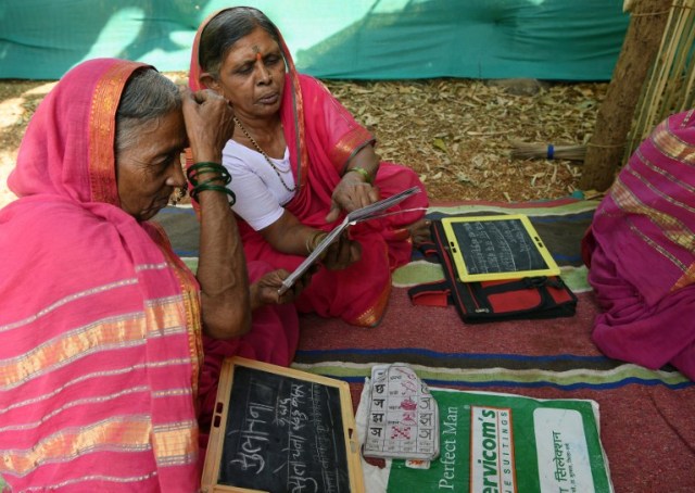 This photo taken on March 1, 2017 shows Indian grandmother Kantabai More (R), 70, explaining a lesson to her classmate Sulochona Kedar, 68, during a class at Aajibaichi Shala, or "school for grannies" in the local Marathi language, in Phangane village in Maharashtra state's Thane district, some 125km northeast of Mumbai. They wear uniforms, carry satchels, and eagerly recite the alphabet in class, but the students here are different -- this is a "school for grannies". Deprived of an education as children, the women -- most of whom are widows and aged between 60 and 90 -- are finally fulfilling a life-long dream to become literate through this unique initiative near Mumbai. / AFP PHOTO / Indranil MUKHERJEE / TO GO WITH "India-education-women-school,FEATURE" by Peter HUTCHISON