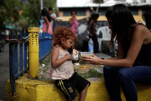 Una voluntaria de la iniciativa benéfica Make the Difference (Haz La Diferencia) regala una taza de sopa y una arepa a un niño sin hogar en una calle de Caracas, Venezuela el 5 de marzo de 2017. Fotografía tomada el 5 de marzo de 2017. REUTERS / Marco Bello