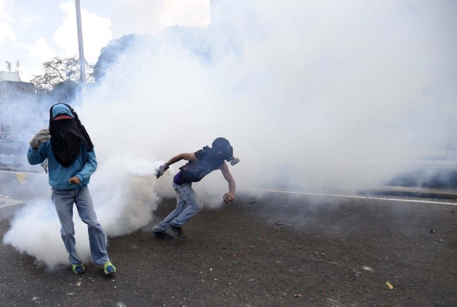 A demonstrator(R) against Nicolas Maduro's government returns a tear gas during clashes with riot police at eastern Caracas on April 8, 2017. The opposition is accusing pro-Maduro Supreme Court judges of attempting an internal "coup d'etat" for attempting to take over the opposition-majority legislature's powers last week. The socialist president's supporters held counter-demonstrations on Thursday, condemning Maduro's opponents as "imperialists" plotting with the United States to oust him. / AFP PHOTO / JUAN BARRETO