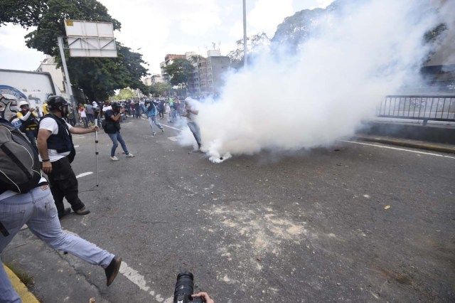Demonstrators against Nicolas Maduro's government are seen amid a tear gas cloud during clashes with riot police in Caracas on April 8, 2017. The opposition is accusing pro-Maduro Supreme Court judges of attempting an internal "coup d'etat" for attempting to take over the opposition-majority legislature's powers last week. The socialist president's supporters held counter-demonstrations on Thursday, condemning Maduro's opponents as "imperialists" plotting with the United States to oust him. / AFP PHOTO / JUAN BARRETO