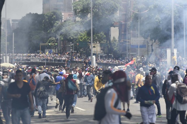 Demonstrators against Nicolas Maduro's government are seen amid a tear gas cloud during clashes with riot police in Caracas on April 8, 2017. The opposition is accusing pro-Maduro Supreme Court judges of attempting an internal "coup d'etat" for attempting to take over the opposition-majority legislature's powers last week. The socialist president's supporters held counter-demonstrations on Thursday, condemning Maduro's opponents as "imperialists" plotting with the United States to oust him. / AFP PHOTO / JUAN BARRETO