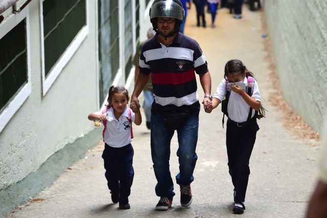 A schoolgirl covers her nose and mouth to avoid breathing tear gas shot by police at opponents of Venezuelan President Nicolas Maduro marching in Caracas on April 26, 2017. Protesters in Venezuela plan a high-risk march against President Maduro Wednesday, sparking fears of fresh violence after demonstrations that have left 26 dead in the crisis-wracked country. / AFP PHOTO / RONALDO SCHEMIDT