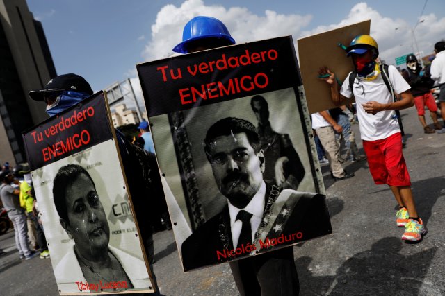 Demonstrators carry signs with images of President Nicolas Maduro and National Electoral Council (CNE) President Tibisay Lucena with that reads " your real enemy" while rallying against President Nicolas Maduro in Caracas, Venezuela, May 27, 2017. REUTERS/Carlos Garcia Rawlins