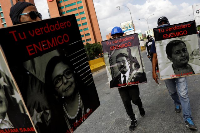 Demonstrators carry signs with images of President Nicolas Maduro (C), National Electoral Council (CNE) President Tibisay Lucena and Minister of Foreign affairs Delcy Rodriguez (L) that reads "your real enemy" while rallying against President Nicolas Maduro in Caracas, Venezuela, May 27, 2017. REUTERS/Carlos Garcia Rawlins