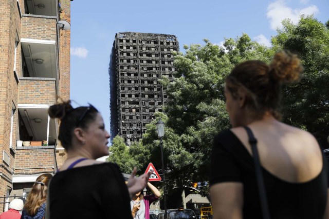 Two women talk in the shadow of Grenfell Tower, a residential tower block that was gutted in a fire in west London on June 15, 2017. Firefighters searched for bodies today in a London tower block gutted by a blaze that has already left 17 dead, as questions grew over whether a recent refurbishment contributed to the fire. / AFP PHOTO / Tolga AKMEN