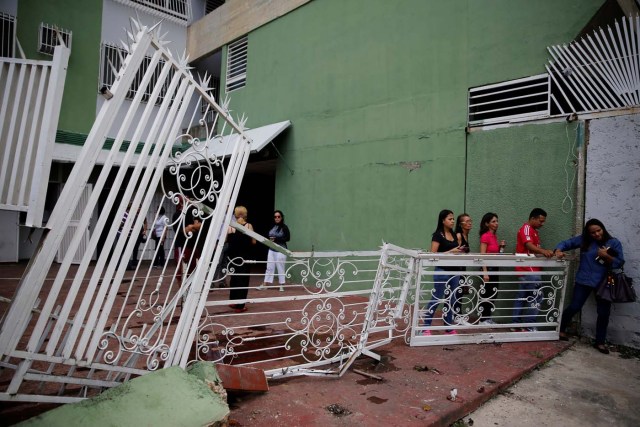People walk past the broken fencing of a building after opposition supporters and security forces clashed in and outside the building on Tuesday according to residents, in Caracas, Venezuela June 14, 2017. REUTERS/Ivan Alvarado