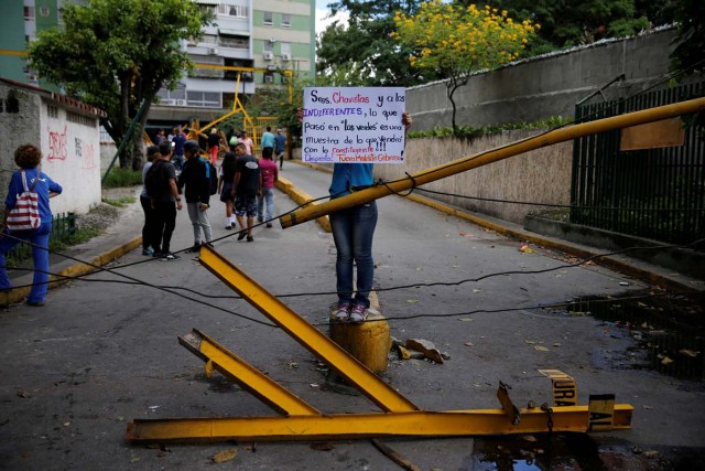 A woman holds a sign while standing on a broken gate after opposition supporters and security forces clashed in and outside residential buildings on Tuesday according to residents, in Caracas, Venezuela June 14, 2017. The sign reads "Gentlemen Chavistas and to the indifferent, what happened in Los Verdes (in reference to the neighbourhood and building), is a sample of what will come with the constituent. Wake up! Out damn govenment!" REUTERS/Ivan Alvarado