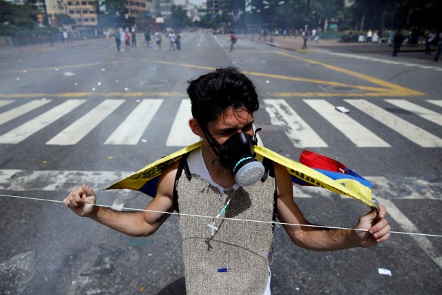 A demonstrator wears a tear-gas mask and holds a Venezuelan flag over his shoulders at a road block during a rally against Venezuelan President Nicolas Maduro's government, in Caracas, Venezuela July 10, 2017. REUTERS/Carlos Garcia Rawlins