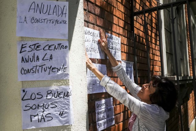 CAR03. CARACAS (VENEZUELA), 24/07/2017.- Una mujer pega carteles en rechazo a la Asamblea Constituyente hoy, lunes 24 de julio de 2017, en una verja de Caracas (Venezuela). Venezuela inicia hoy la semana decisiva para la elección de la Asamblea Nacional Constituyente convocada por el presidente, Nicolás Maduro, con los oficialistas entrando en la recta final de su campaña en medio de protestas y llamados a paro de los opositores en rechazo a esos comicios. EFE/Miguel Gutiérrez