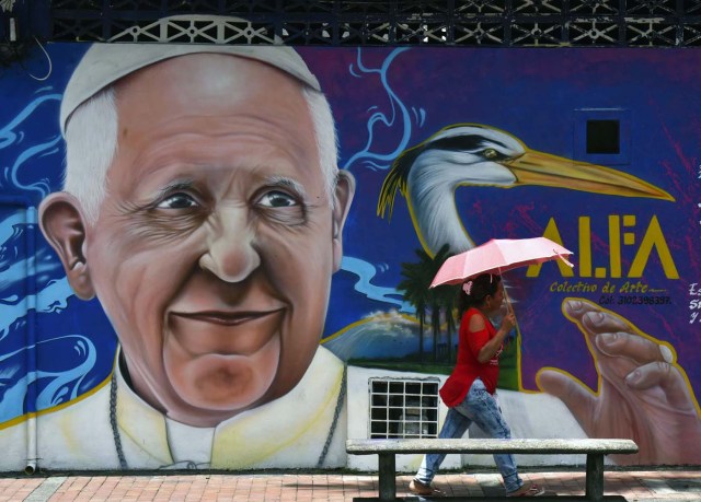 A passer-by walks past a painting of Pope Francis in Villavicencio, Meta, Colombia - where he will give mass during his upcoming visit to Colombia - on August 28, 2017.  Pope Francis will make a special four-day visit to Colombia, from September 6-11, to add his weight to the process of reconciliation between the government and the FARC. / AFP PHOTO / LUIS ACOSTA