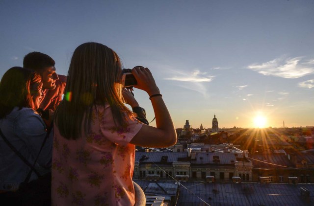 Tourists look at the city during a visit to the first official tour of the roofs in St. Petersburg on August 11, 2017.  / AFP PHOTO / OLGA MALTSEVA