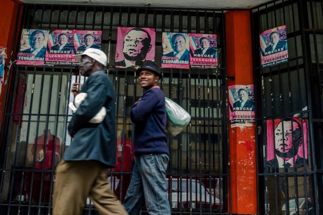Harare residents walk past campaign posters portraying Zimbabwe Opposition and Movement for Democratic Change leader Morgan Tsvangirai in Harare on November 15, 2017. Zimbabwe's military appeared to be in control of the country on November 15 as generals denied staging a coup but used state television to vow to target "criminals" close to President Mugabe. / AFP PHOTO / -