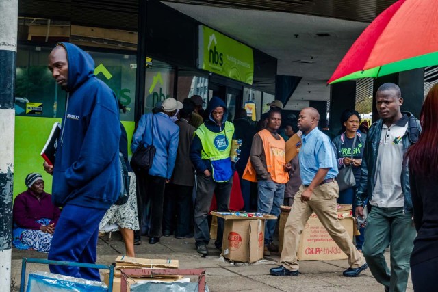 Residents walk in a street as others queue outside a bank in Harare on November 15, 2017. Zimbabwe's military appeared to be in control of the country on November 15 as generals denied staging a coup but used state television to vow to target "criminals" close to President Mugabe. / AFP PHOTO / -