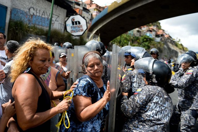 People confront riot police during a protest against the shortage of food, amid Fuerzas Armadas avenue in Caracas on December 28, 2017. As Venezuelans protest in Caracas demanding the government's prommised pork -the main dish of the Christmas and New Year's dinner-, President Nicolas Maduro attributes the shortage to international sabotage. / AFP PHOTO / FEDERICO PARRA