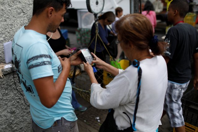 Una mujer usa un dispositivo de punto de venta (POS) en un mercado callejero de verduras en Caracas, Venezuela el 19 de diciembre de 2017. Foto tomada el 19 de diciembre de 2017. REUTERS / Marco Bello