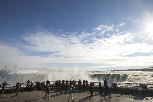 Tourists take photos of the Horseshoe Falls in Niagara Falls, Ontario on January 3, 2018. The cold snap which has gripped much of Canada and the United States has nearly frozen over the American side of the falls. / AFP PHOTO / Geoff Robins