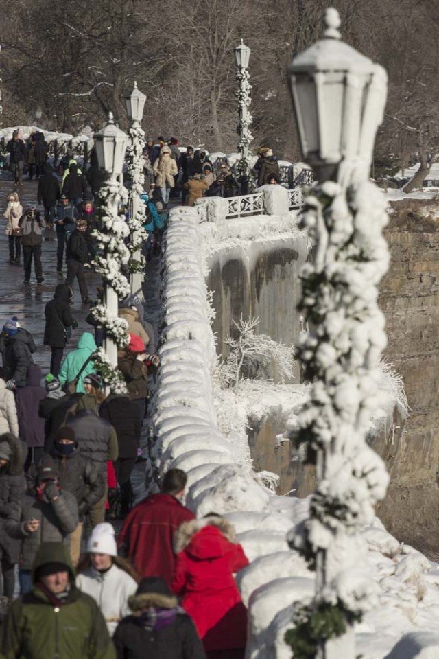 Tourists gather along the frozen railings near the Horseshoe Falls in Niagara Falls, Ontario on January 3, 2018. The cold snap which has gripped much of Canada and the United States has nearly frozen over the American side of the falls. / AFP PHOTO / Geoff Robins