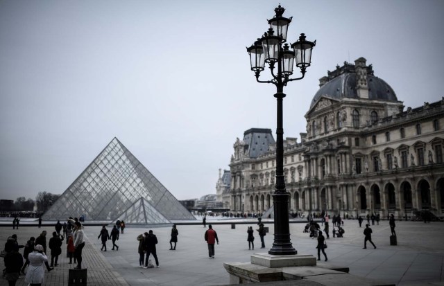 People walk towards the the Louvre Pyramid in Paris on February 19, 2018. / AFP PHOTO / STEPHANE DE SAKUTIN