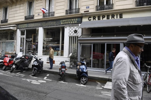La gente camina en la calle Monsigny como una bandera nacional francesa colgada de una ventana, el 13 de mayo de 2018 en París, en el sitio donde un matón fue asesinado por la policía después de que mató a un hombre e hirió a otras cuatro en la víspera en el zona. / AFP PHOTO / Eric FEFERBER